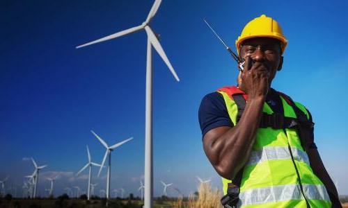 A person in a vest 和 hard hat in front of a wind turbine