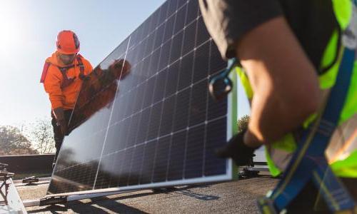 Two workers carrying a solar panel across a rooftop.